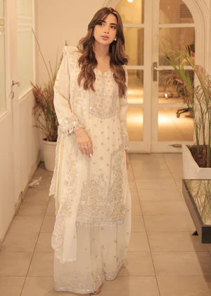 Woman in a white embroidered outfit standing in a well-lit room with plants.
