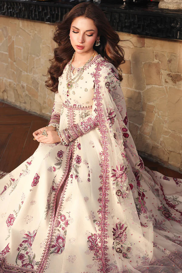 Woman wearing a white and pink embroidered traditional outfit in a stone-walled room.