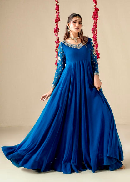 Woman in a blue gown with intricate details standing against a neutral background