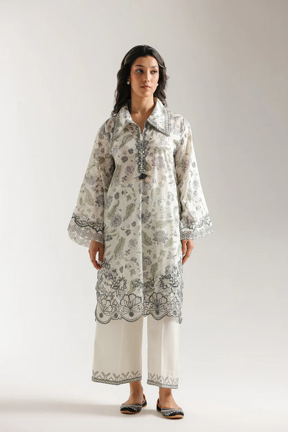 Woman wearing a patterned long shirt with matching pants on a plain background