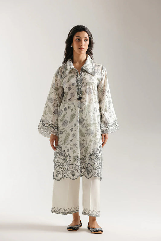 Woman wearing a patterned long shirt with matching pants on a plain background
