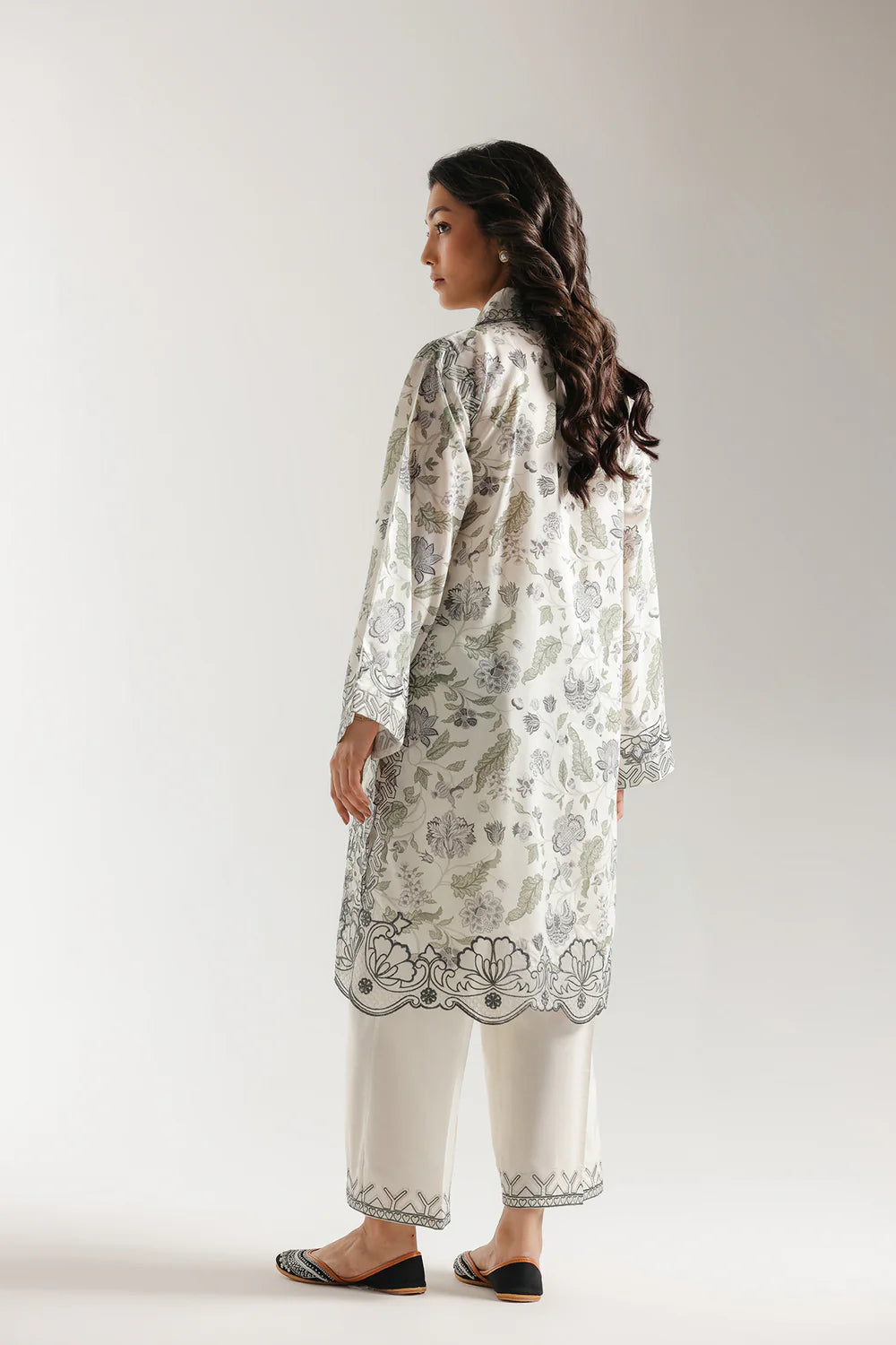 Woman wearing a floral embroidered kurta with white pants on a plain background