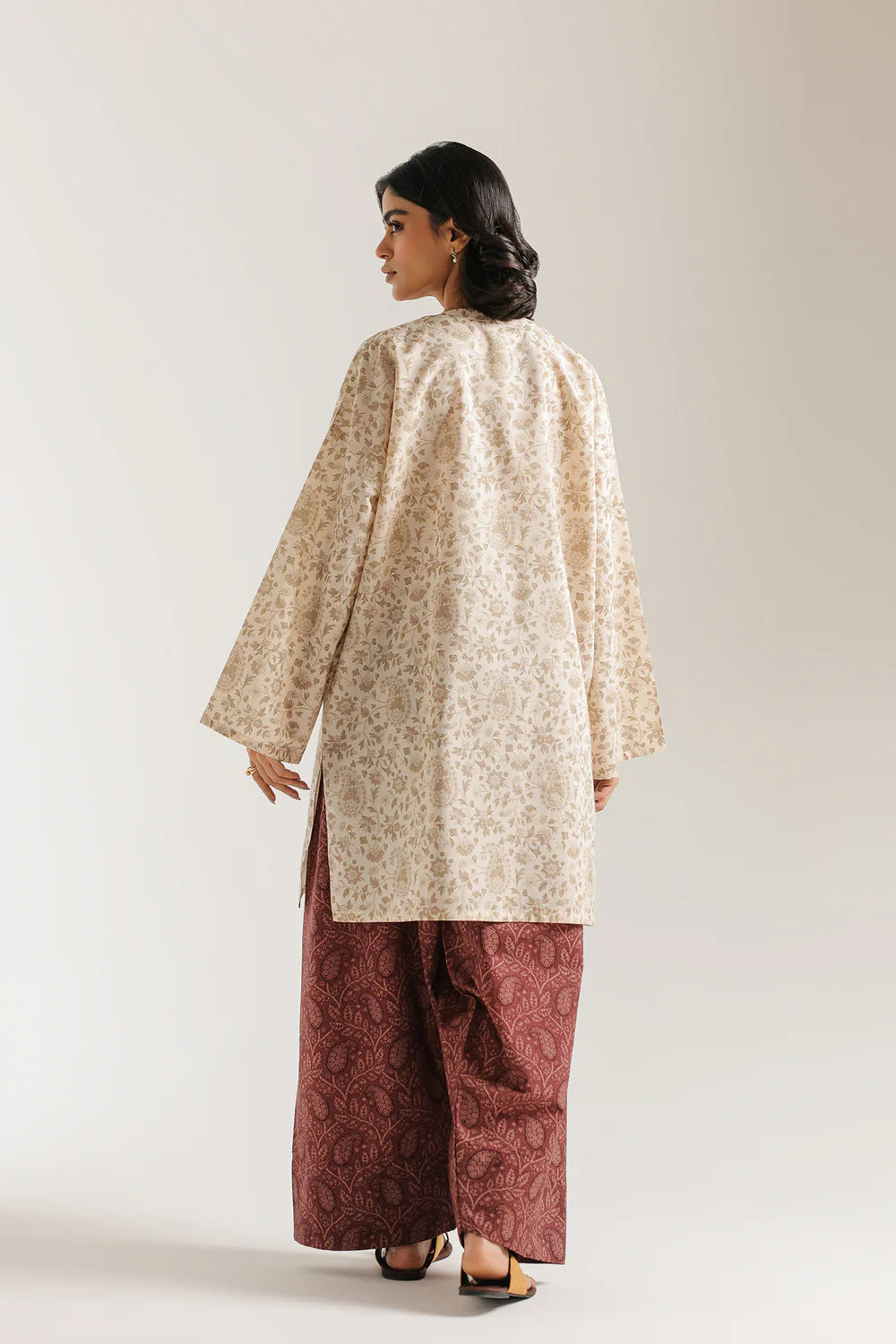 Woman wearing a beige floral top and maroon pants on a white background