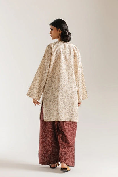 Woman wearing a beige floral top and maroon pants on a white background
