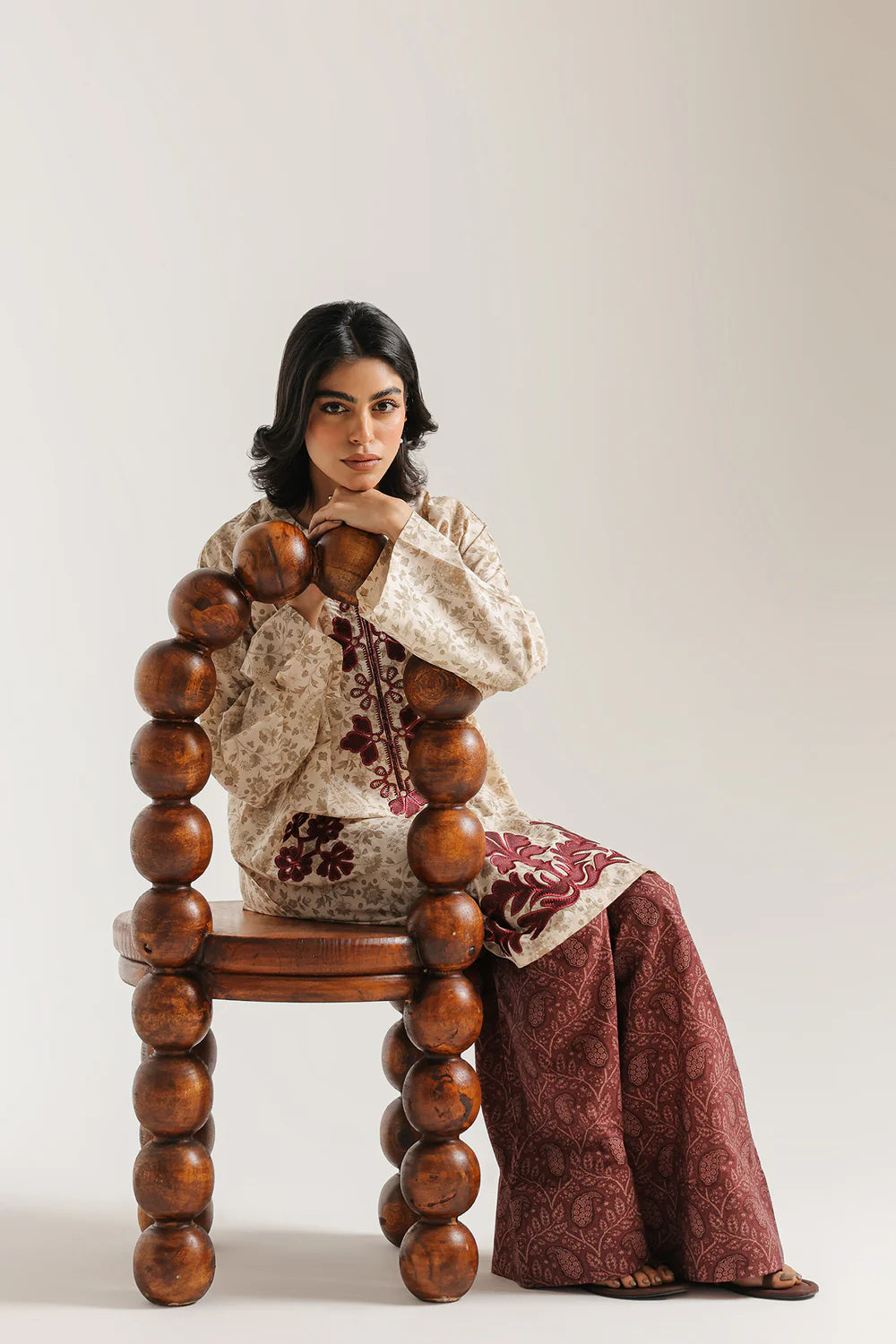 Woman sitting on a wooden chair with spherical legs against a plain background