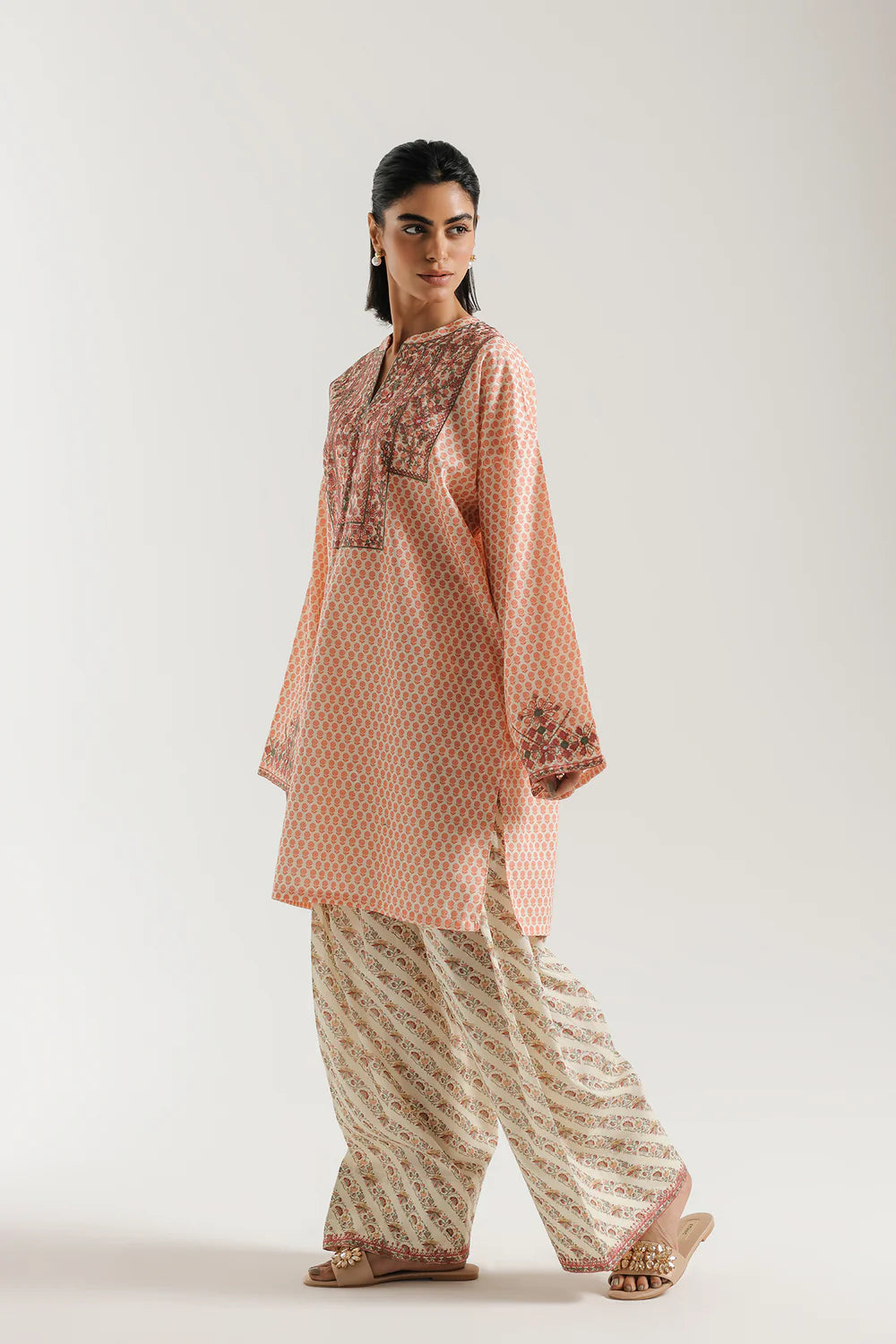 Woman wearing a peach-colored kurta with intricate embroidery and white pants on a light background