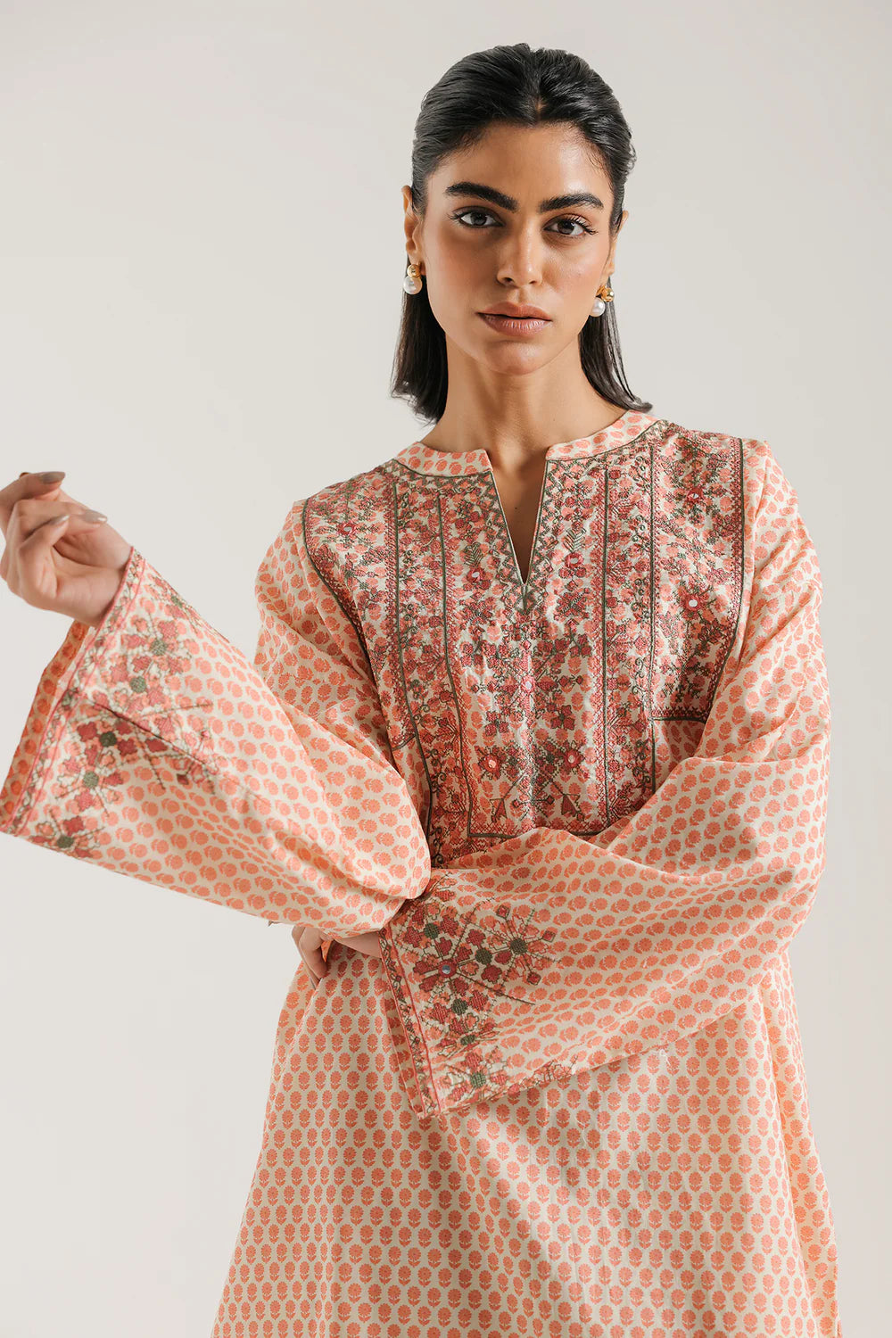 Woman wearing a patterned pink and red kurta against a plain background