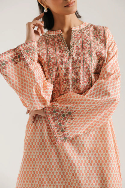 Woman wearing a patterned dress with bell sleeves on a plain background