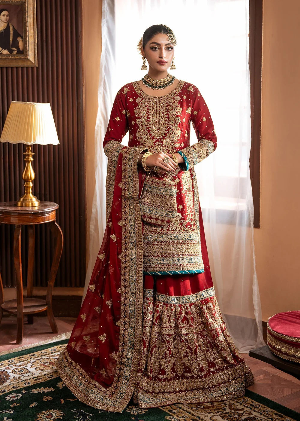 Woman in traditional red and gold embroidered outfit standing in a room with decor elements.