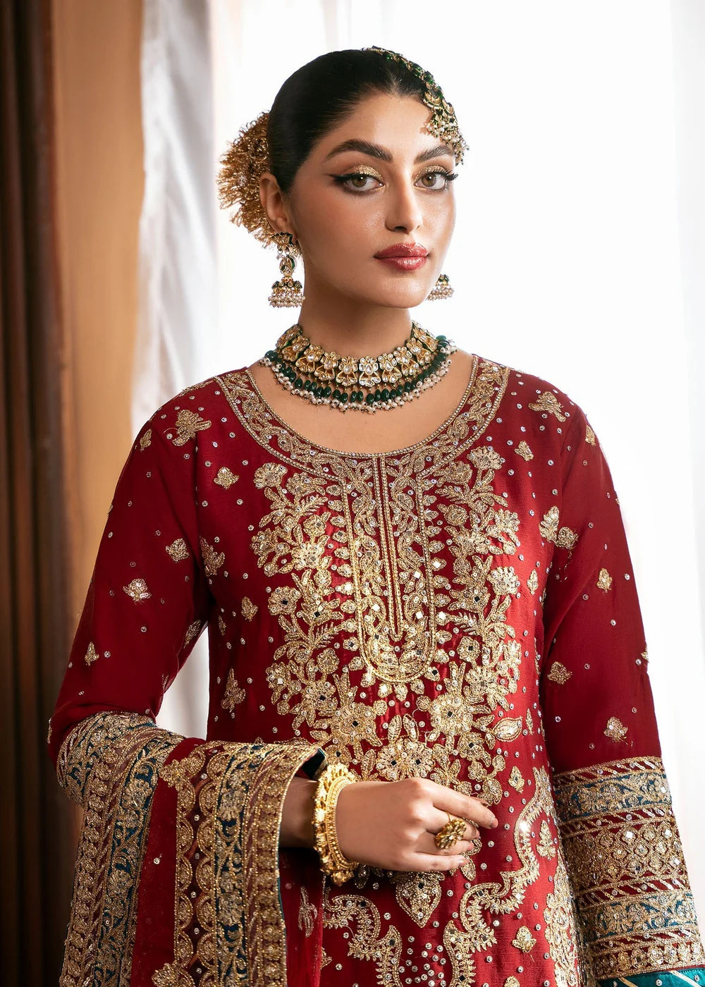 Woman wearing a red embroidered traditional outfit with gold jewelry.