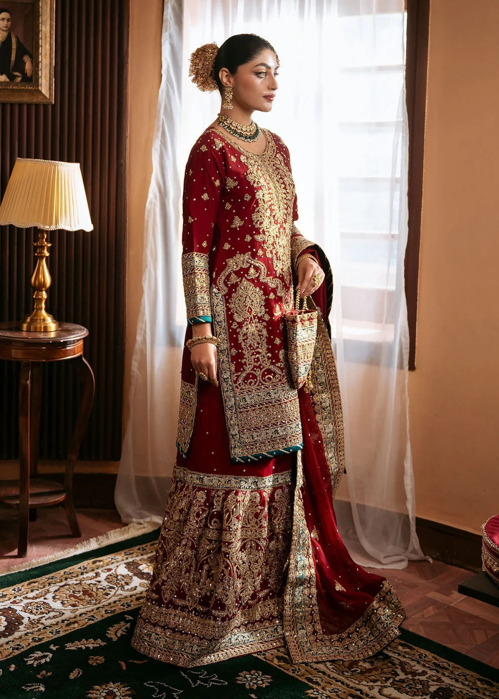 Woman in traditional red and gold embroidered outfit standing in a room with decor elements.