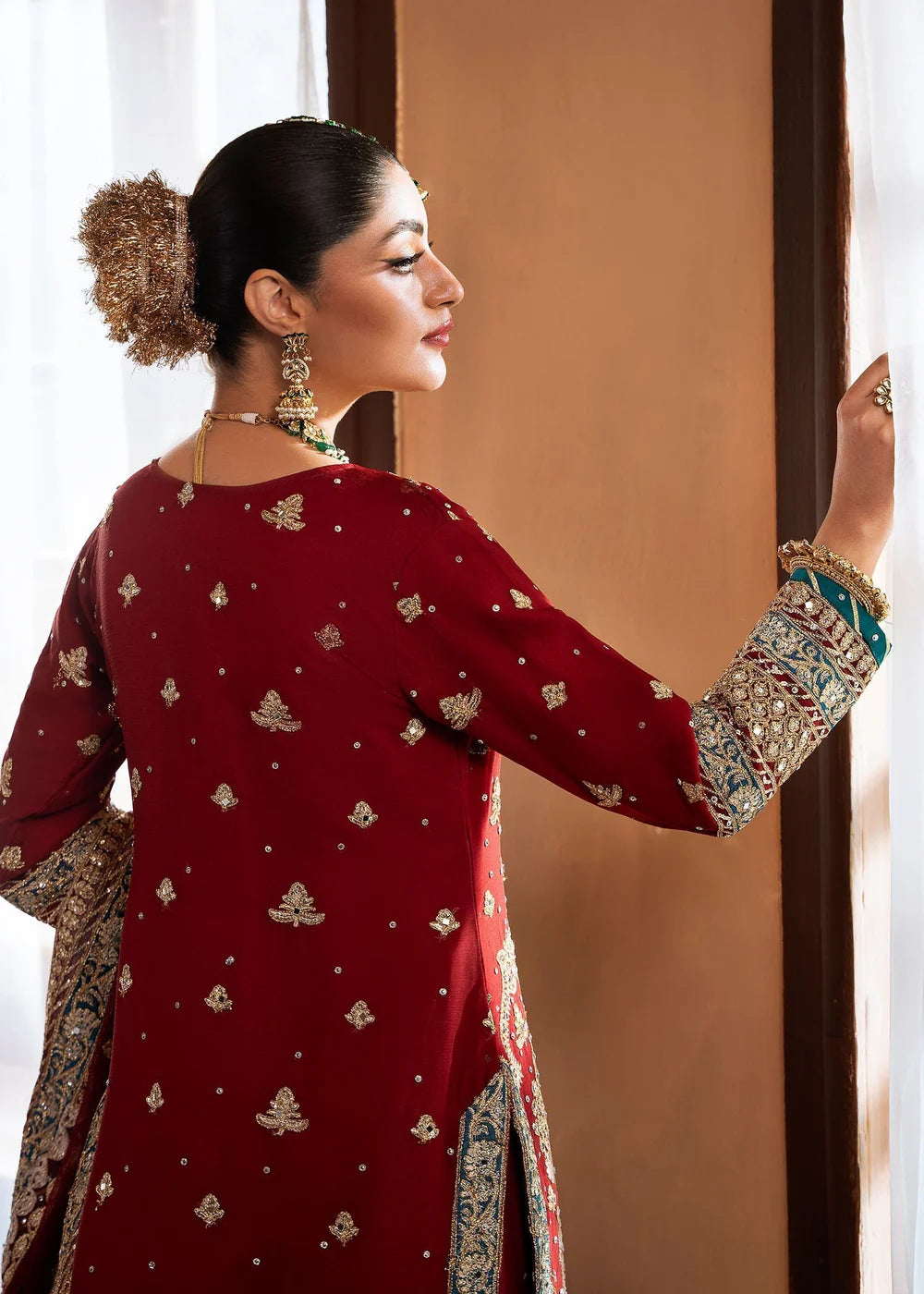 Woman in a red traditional outfit with intricate patterns, standing indoors.