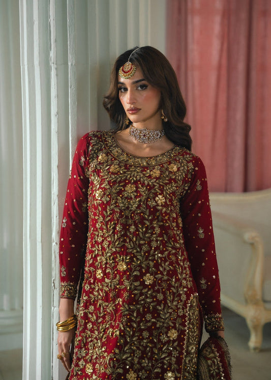 Woman in a red and gold embroidered traditional outfit standing indoors.