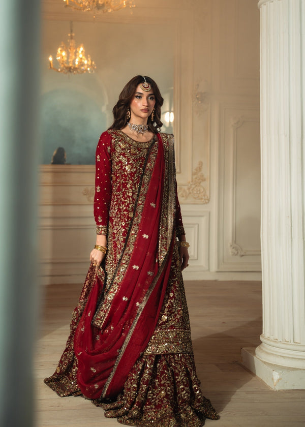 Woman in a traditional embroidered outfit with red and gold colors in an elegant interior setting.