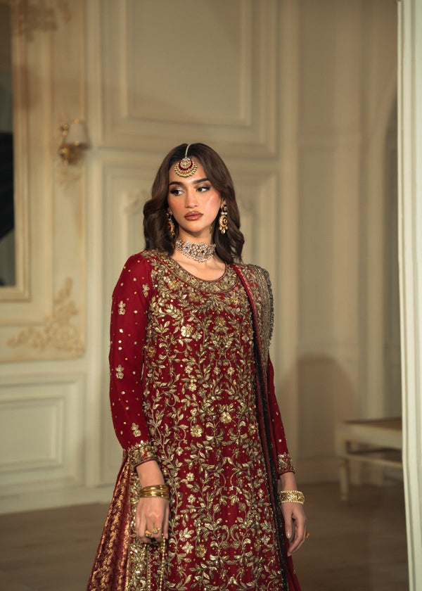 Woman in a red and gold traditional outfit with jewelry in an elegant room.