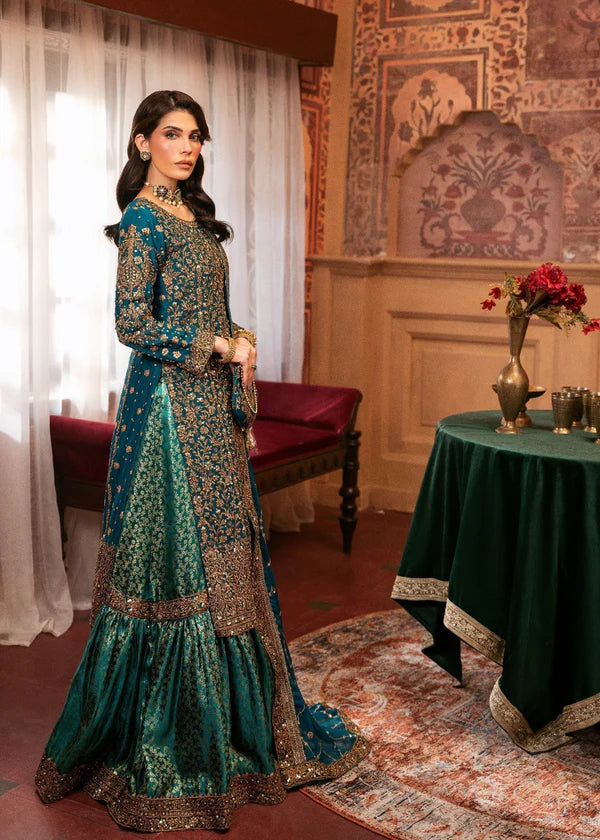 Woman in a traditional teal and gold outfit standing in an ornate room with a table and flowers.