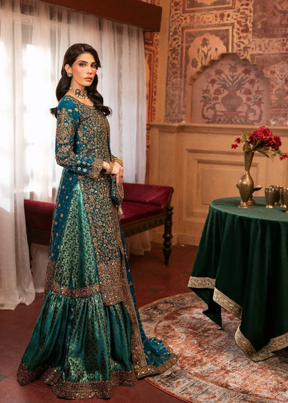 Woman in a traditional teal and gold outfit standing in an ornate room with a table and flowers.